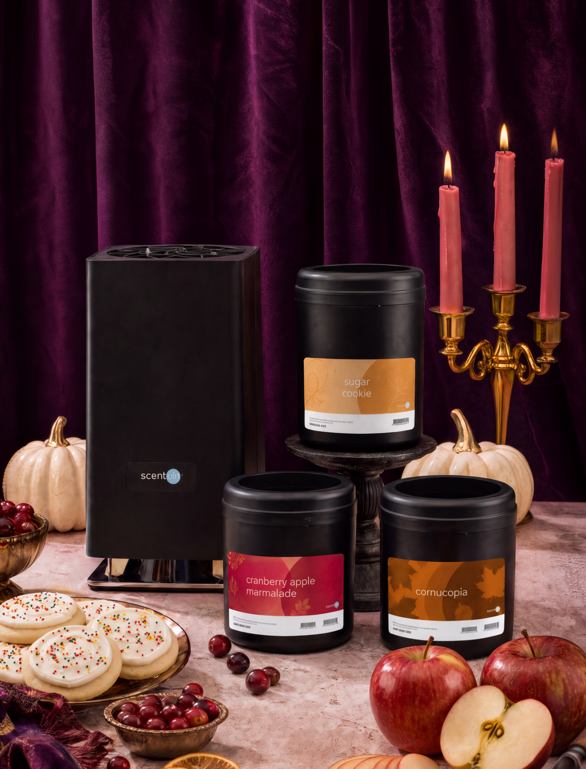 Three black Whisper PRO Cartridges with autumn-themed labels are displayed alongside a black scent diffuser on a styled tabletop with pumpkins, apples, cookies, cranberries, and a purple velvet backdrop with lit candles.
